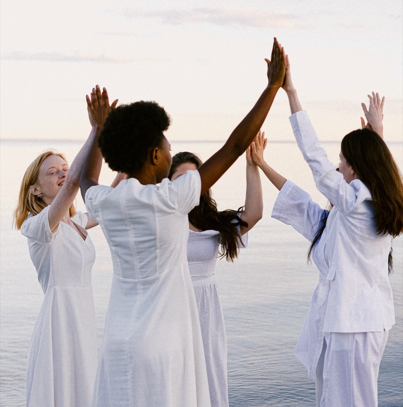 Frauen in Weiß am Meer, die Hände zusammen erhoben